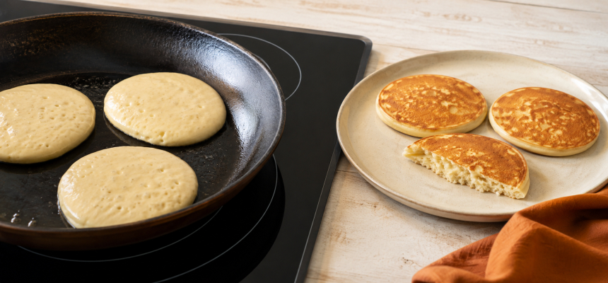 Fluffige Pancakes beim Braten in der Pfanne und fertige Pancakes auf dem Teller